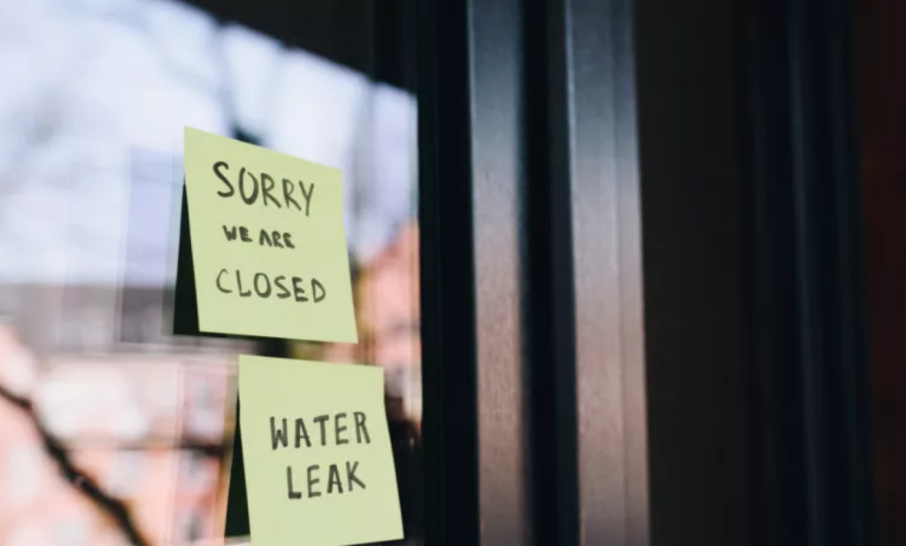 Closed doors of a business with a sign reading 'Closed due to water leak,' indicating the closure caused by a water leak.